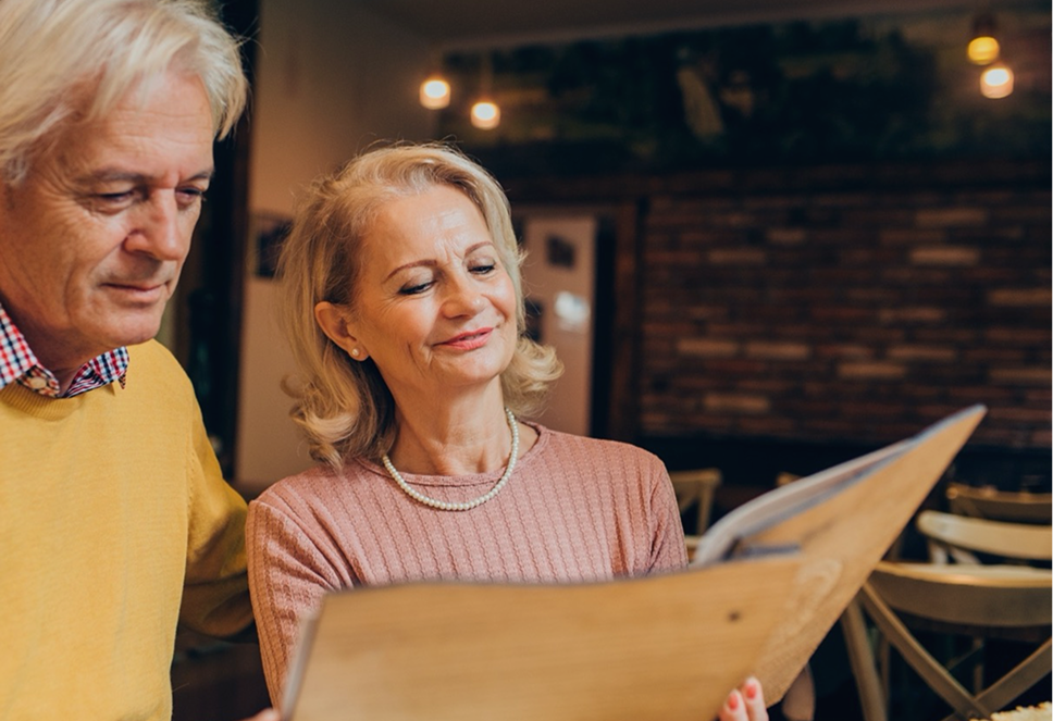 A middle-aged woman reading a book indoors without glasses, representing improved intermediate and near vision