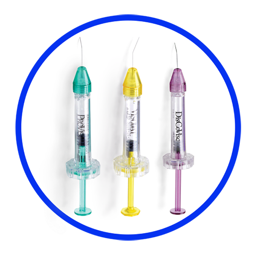 A close-up shot of three tubes of Alcon Ophthalmic Viscosurgical Devices. The tube with the purple cap is labeled DisCoVisc, the tube with the yellow cap is labelled VISCOAT, and the tube with the green cap is labelled PROVISC. Behind the tubes there is a surgeon wearing a medical mask and surgical scrubs.