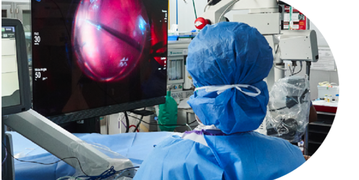 An image of a group of surgeons in an operating room with a patient undergoing surgery. An NGENUITY screen shows a close-up view of the surgery to the surgeons in the room.