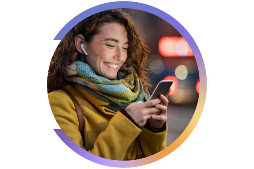 Femme souriante avec manteau jaune et foulard, regardant son téléphone tout en portant des écouteurs sans fil