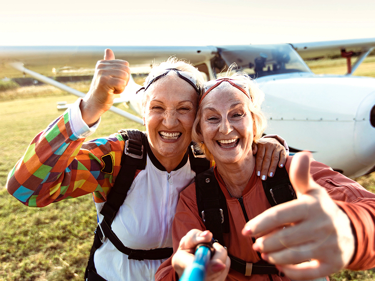 Two women taking a selfie with an airplane in the background.