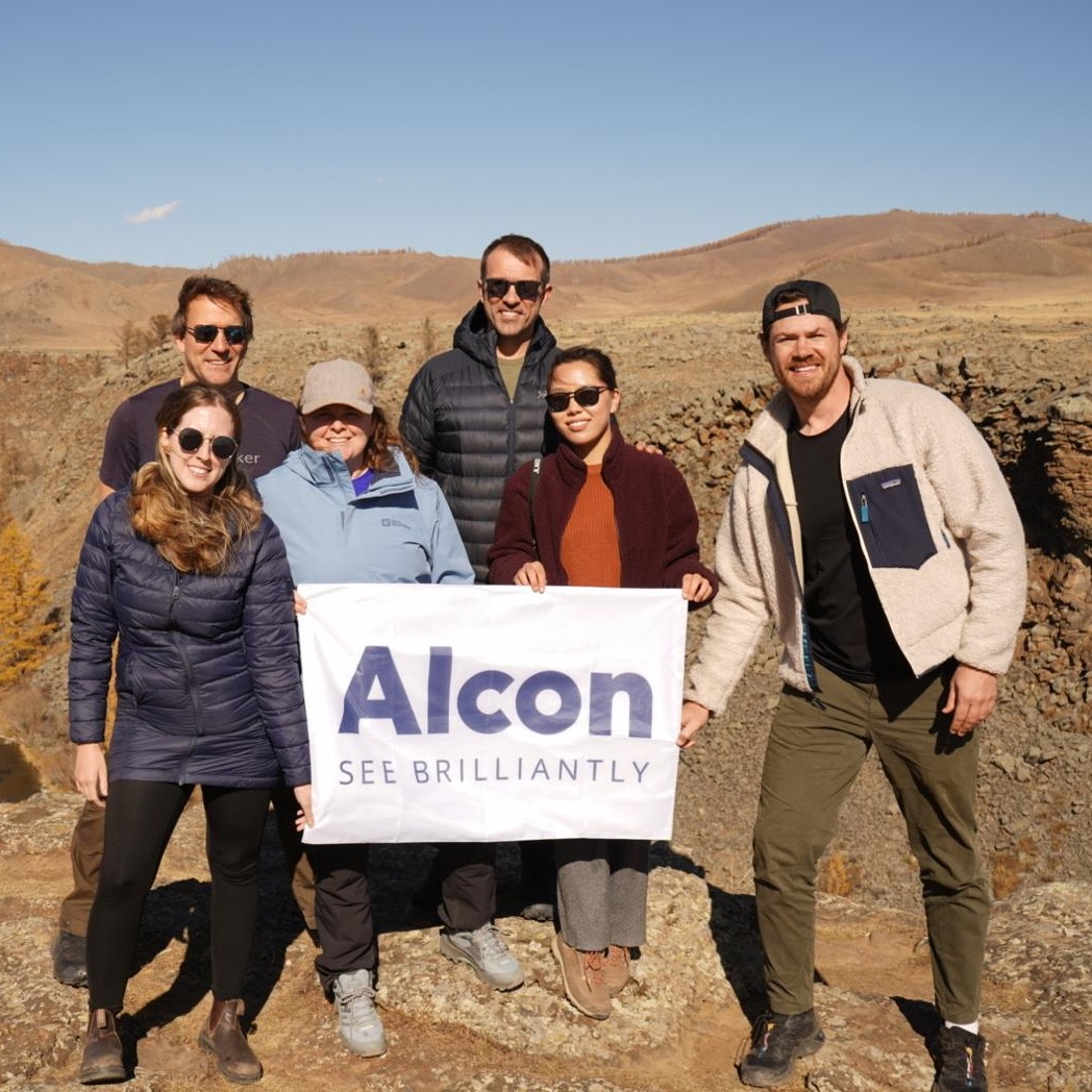 group of volunteers standing outside holding sign reading: Alcon - See Brilliantly