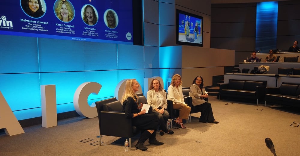 Four women sitting in chairs on stage at conference