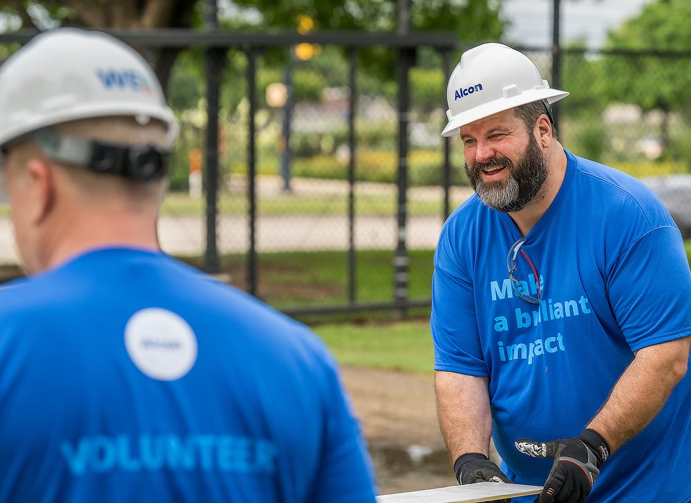 Two male Alcon volunteers working in blue t-shirts and hard hats.