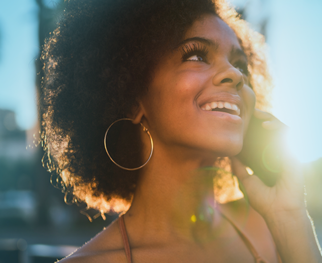 Woman on phone in sunlight smiling looking up